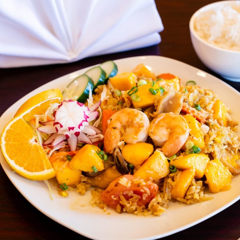 Thai mango fried rice with shrimp, chicken, and vegetables, garnished with orange and radish.