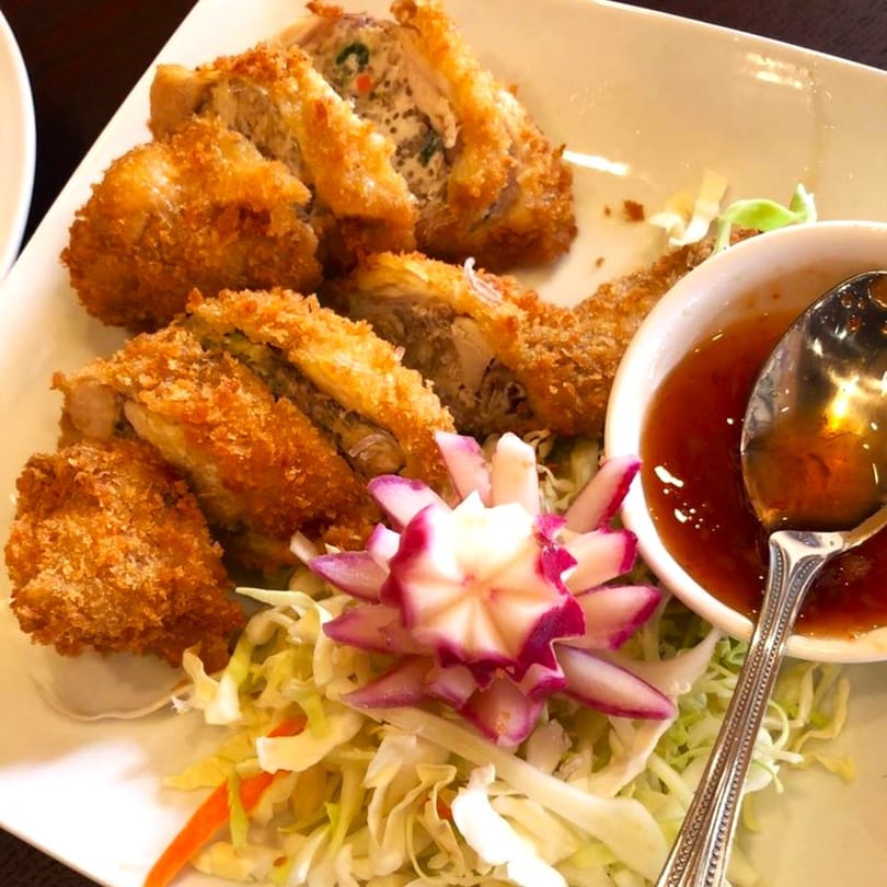 Crispy fried Thai chicken rolls with a side of sweet chili sauce and shredded cabbage.