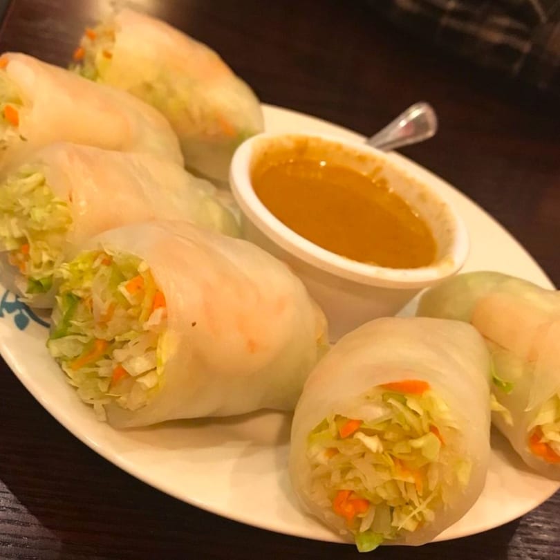 Fresh Thai spring rolls filled with cabbage and carrots, served with a side of peanut sauce.